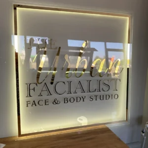 Elegant acrylic sign featuring "The Urban Facialist" branding with a luxurious gold finish and soft backlighting, perfect for a face and body studio.