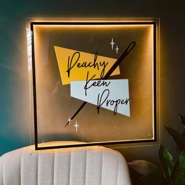 Stylish acrylic sign featuring the "Peachy Keen Proper" branding with geometric accents and warm golden backlighting, perfect for modern spaces.