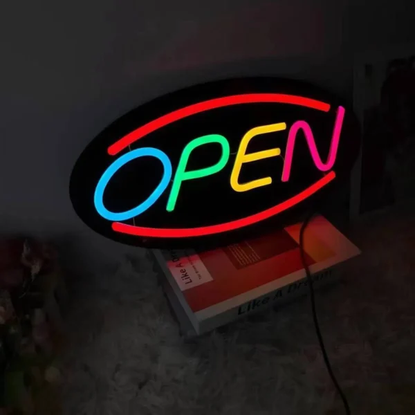 An eye-catching Neon Open Sign with OPEN glowing in red, blue, yellow, and green LED lights rests on the book Like A Dream, against a dark background.