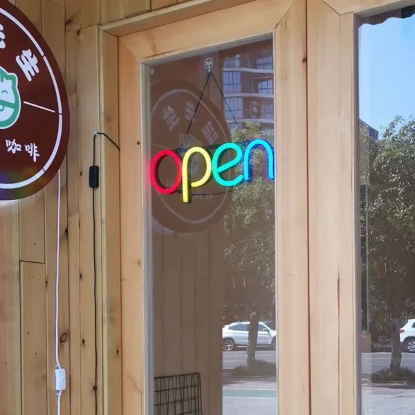 Vibrant rainbow-colored neon "OPEN" sign hanging on a shop's glass door, creating a welcoming and modern storefront look.