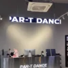 A modern dance studio reception features a sleek counter with a PAR-T DANCE sign and a Full Color LED Digital Display Sign, showcasing vibrant visuals.